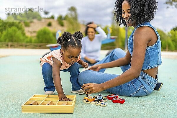 Little african girl messing with toys from a box playing with family in an outdoor park