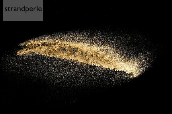 Golden sand explosion isolated on black background. Abstract sand cloud. Golden colored sand splash against dark background. Yellow sand fly wave in the air