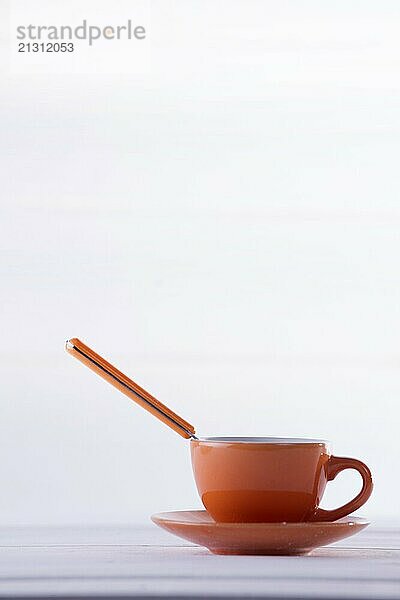 Cup of coffee on orange background and white spoon