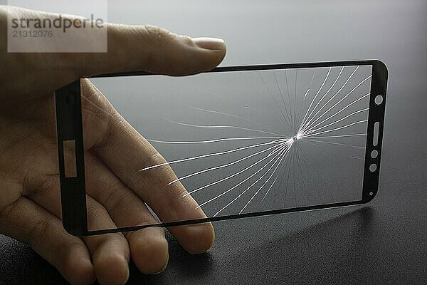 Broken protective glass of smartphone with cracks in hand on black background. Broken glass protection smartphone