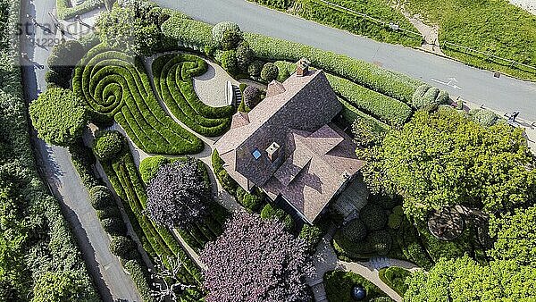 17.05.2023 Etretat France Drone perspective on the gardens of Etratat (Les Jardins D'Etretat) with house: fantastic topiary curves of bushes and zigzags of a motorway. Two trees with red leaves