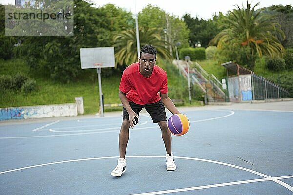 Portrait of a young african man dribbling a basketball ball at the outdoor courtyard