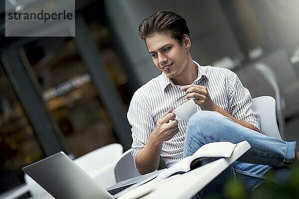 Handsome caucasian young man working on laptop and smiling while enjoying coffee in cafe