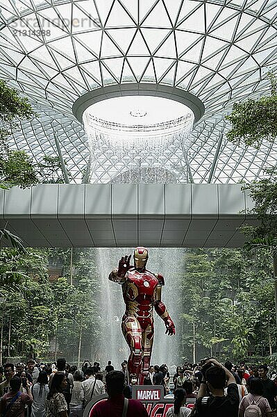 16.07.2023  Singapore  Republic of Singapore  Asia  Visitors and air travellers in the indoor garden of the Shiseido Forest Valley with the rain vortex of the indoor waterfall Rain Vortex in the Jewel Terminal at Singapore Changi Airport. In the foreground is an Iron Man figure from the Marvel film series  Asia