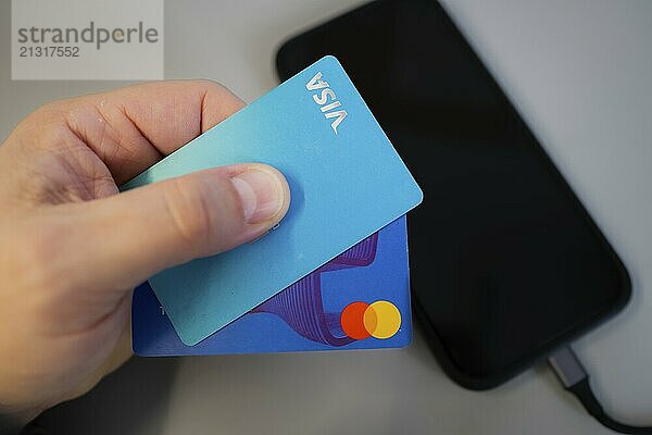 Hand holding two credit cards  for mobile payment  over a black smartphone on a grey background