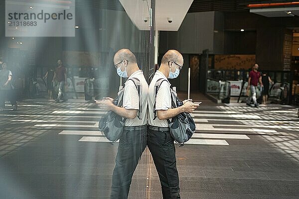 02.04.2020  Singapore  Republic of Singapore  Asia  A man stares at his mobile phone in the Raffles City shopping centre while wearing a mask to protect himself from infection with the pandemic coronavirus  Asia