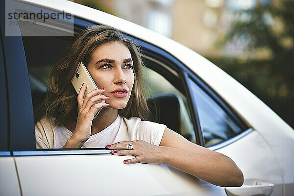 Beautiful woman with phone smiling while sitting on the back seat in the car