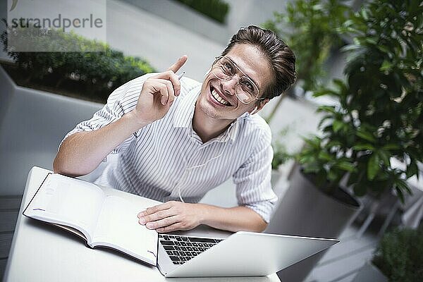 Happy handsome businessman mixes his break and job outdoors  businessman with headphones write some new ideas in notebook sitting in cafe