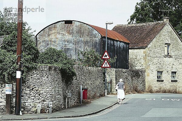 Stow-On-The-Wold  UK  August 12  2015:2015: Traditional english village street with an old woman walking (rear view) with the word SLOW painted on the road