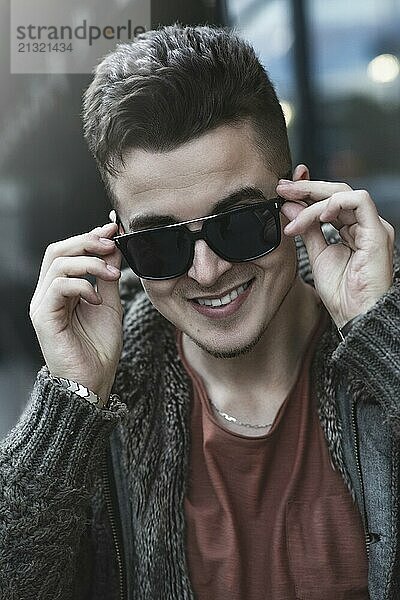 Closeup of cheerful young caucasian man in sunglasses standing and smiling over street background