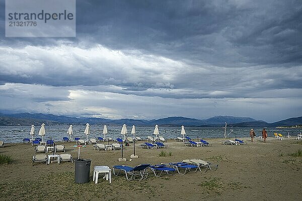 Kalamaki  Corfu  Greece  Sun loungers and parasols on Kalamaki beach in the north-east of the Greek island of Corfu. In the background  mainland Albania with the seaside resort of Saranda. In front forgotten children's toys  bucket and shovel. Price list for parasol and sun lounger hire  Europe