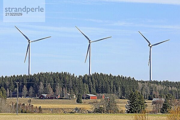 Row of three wind turbines near country village in South of Finland on a sunny day of spring