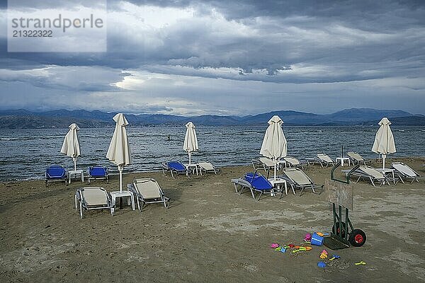 Kalamaki  Corfu  Greece  Sun loungers and parasols on Kalamaki beach in the north-east of the Greek island of Corfu. In the background  mainland Albania with the seaside resort of Saranda. In front forgotten children's toys  bucket and shovel. Price list for parasol and sun lounger hire  Europe