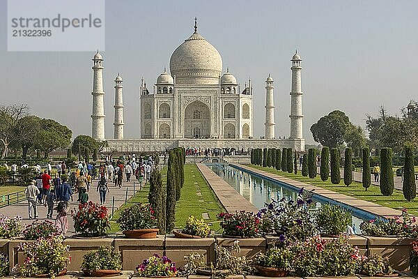 Taj Mahal  the mausoleum built for Mumtaz Mahal by her husband  the Mughal emperor  Shah Jahan. A distant  classic view  with some flowers in the foreground  the water channel reflecting the building  and some colourfully dressed visitors. Photographed in the morning of a mid-April day  the pre-monsoon summer season. Wonder of the World  a UNESCO World Heritage Site  famous landmark and tourist attraction. Agra  Uttar Pradesh  India  Asia