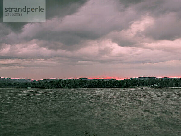 A narrow seam of red sunset light separates the land from the sky above Flagstaff lake in western Maine.