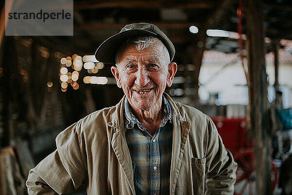 Old man wearing a hat and trench coat smiling.