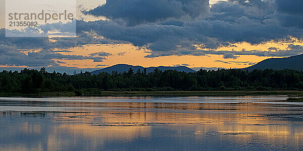 Orange sky and and late evening clouds reflect off Flagstaff Lake in Stratton  Maine at sunset.