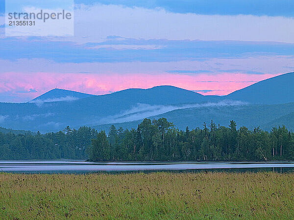 At sunset a magenta sky defines the Western Mountains above the Western Maine mountains on Flagstaff Lake in Stratton  Maine.