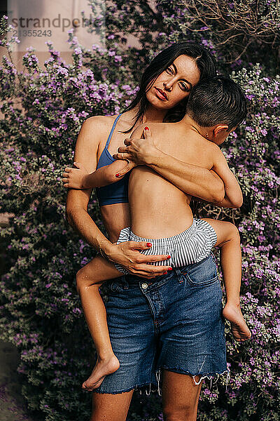 Mother embraces young son against backdrop of purple flowers