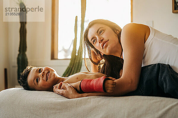 Mother and smiling son relax together on bed  bathed in warm sunlight