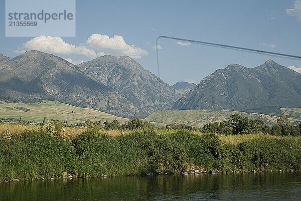 A fly fishing rod in the foreground over a creek with mountains