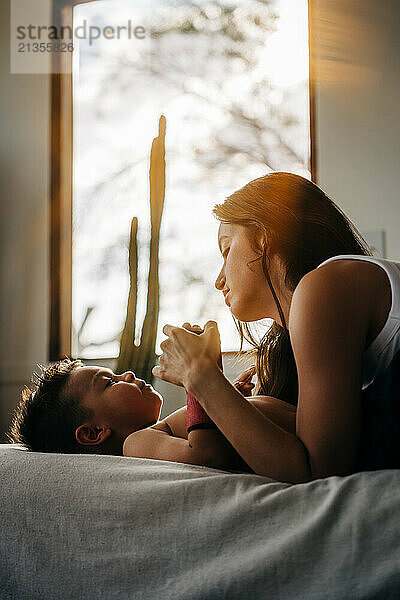 Mother tenderly holds hands with young son in warm  sunlit room