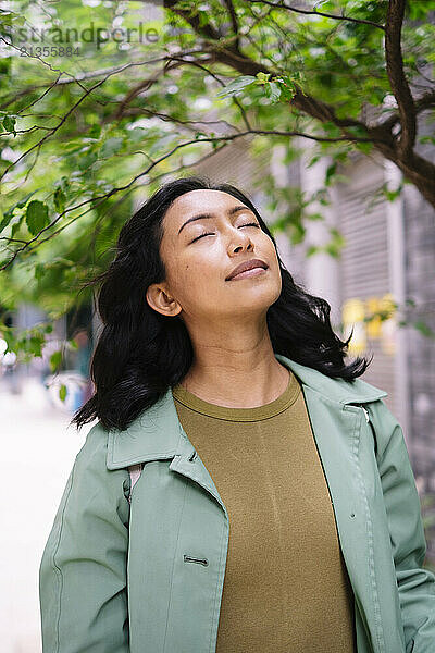 Smiling woman with eyes closed standing near tree