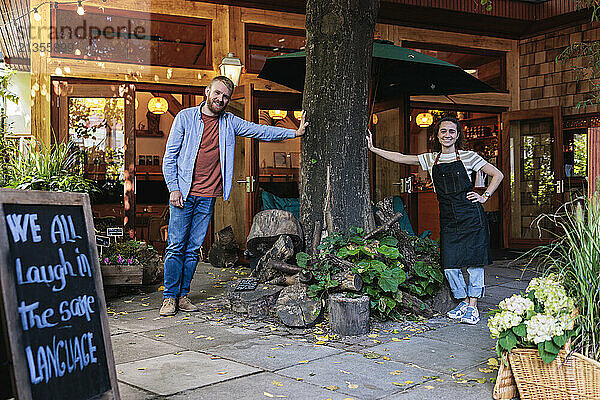 Multiracial cafe owners standing near tree outside coffee shop