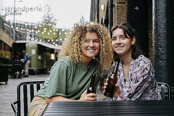 Happy lesbian couple sitting with beer bottles at table