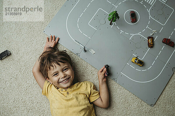 Smiling cute boy lying near toys on floor at home