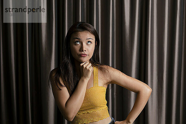 Thoughtful woman with hand on chin in front of curtain at photo booth