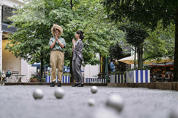 Happy lesbian couple playing boccia balls near trees