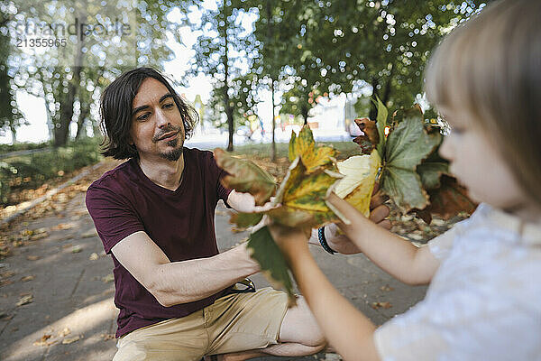 Girl giving autumn leaves to father in public park