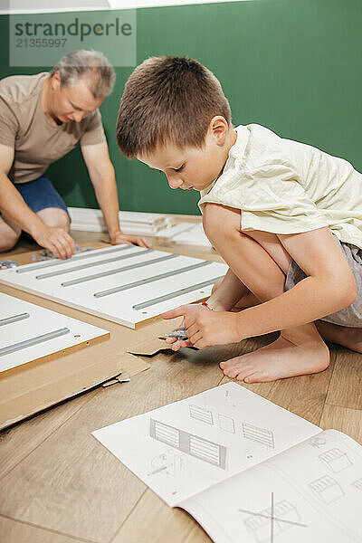 Boy helping father to assemble new furniture at home