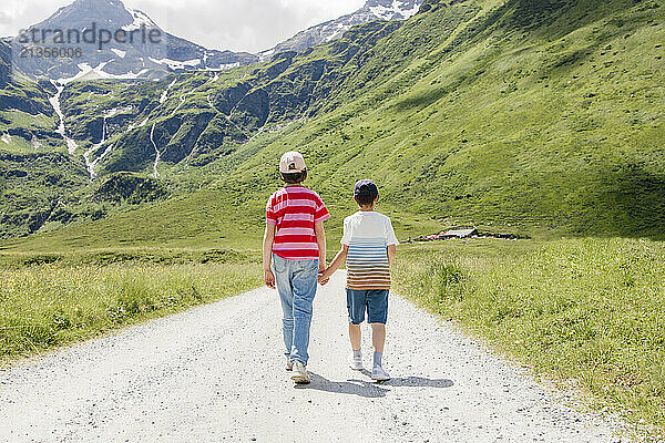 Brother and sister holding hands and walking on footpath in trhe mountains