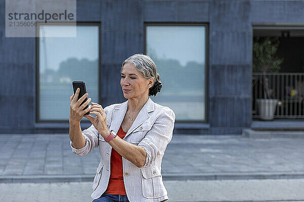 Gray haired woman using smart phone at street