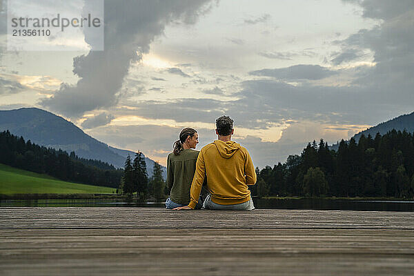 Mature couple sitting on jetty in evening