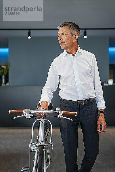 Senior businessman walking with bicycle in office lobby