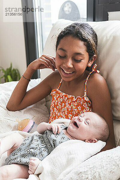 Smiling little sister looking at baby girl at home