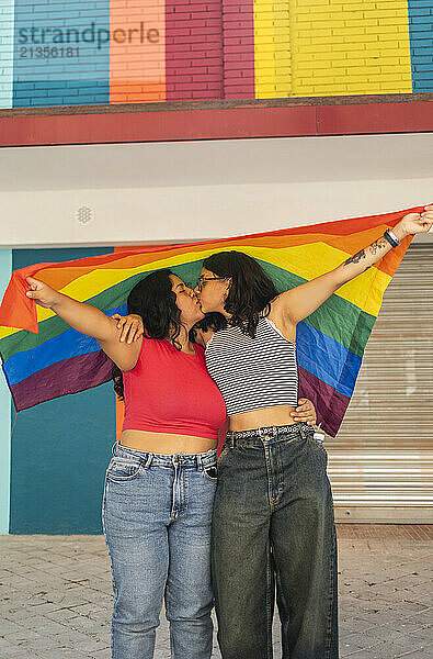 Young gay couple kissing and holding LQBTQIA pride flag