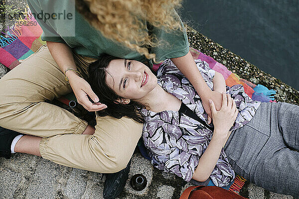 Happy young woman lying on girlfriend's lap near river