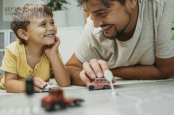 Happy father and son spending leisure time playing with toy cars at home