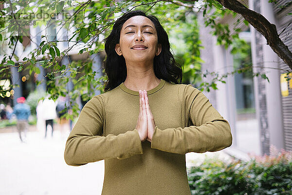 Smiling woman standing with hands clasped near tree