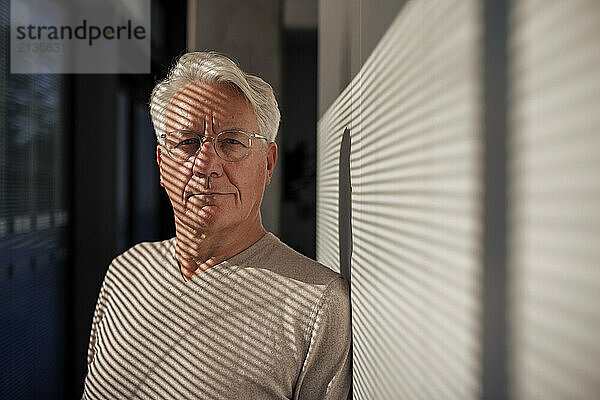 Smiling senior man in sunlight leaning on wall