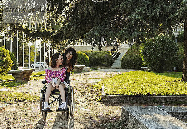 Woman sitting on wheelchair spending leisure time with assistant nurse at park