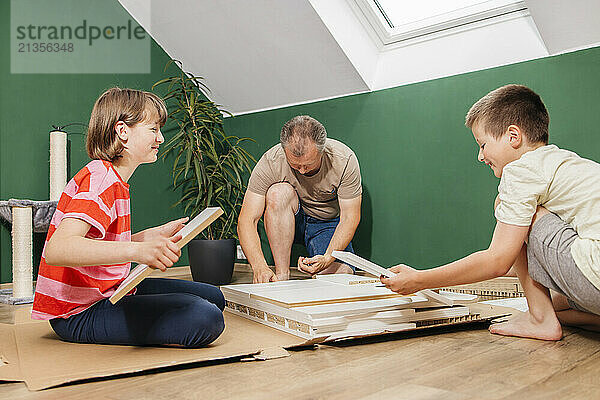 Smiling children and father assembling furniture together at home