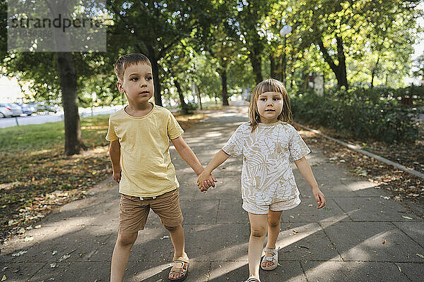 Brother and sister walking together on footpath in park