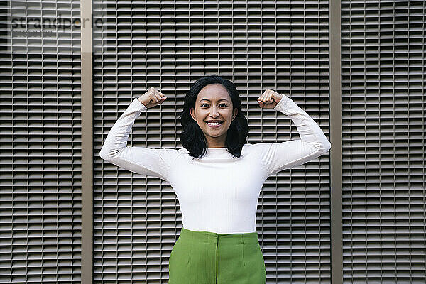 Smiling woman flexing muscles and standing in front of wall