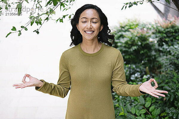 Smiling woman practicing meditation near plants