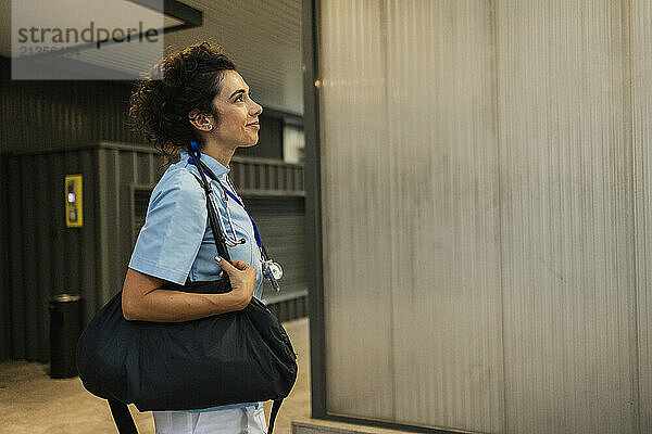 Smiling nurse carrying bag standing at hospital lobby